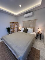 Un dormitorio moderno con una cama grande, una escalera de madera, una planta en maceta y dos lámparas de noche.
