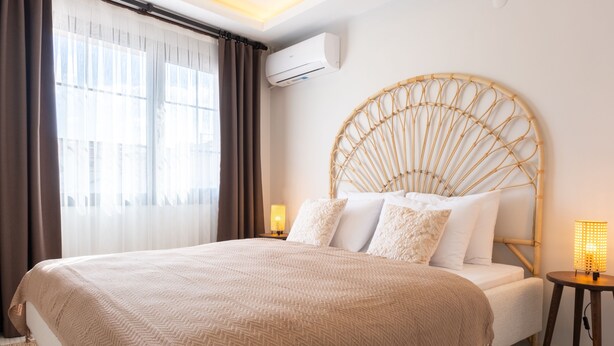 A bedroom with a large bed, a round headboard, a bedside lamp, and an air conditioning unit on the wall.
