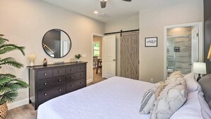 Un dormitorio con cama, cómoda, espejo, ventilador de techo y puerta que da a un baño.