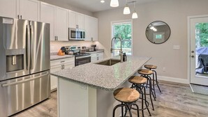Una cocina moderna con electrodomésticos de acero inoxidable, encimeras de granito y taburetes de bar.