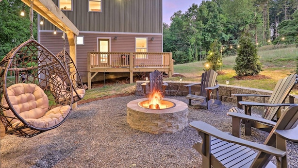 Un patio exterior acogedor con un hogar de piedra, terraza de madera y zona de estar que incluye sillas y una mecedora.