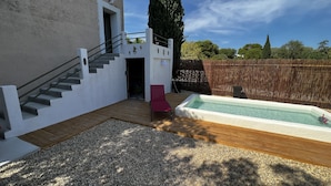 A backyard with a wooden deck, a swimming pool, a red chair, and a staircase leading to a door. - La Maison de vos Vacances (Béziers)