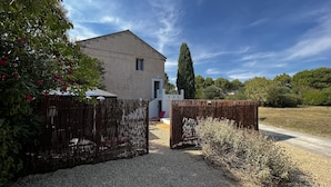 A rustic building with a gravel driveway leading to a wooden gate. - La Maison de vos Vacances (Béziers)