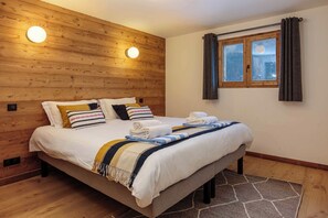 A bed with a white duvet, multiple pillows, and a striped blanket. There is a window with curtains and a view of the outside. - Chalet Gloribel, ski, views, Chamonix All Year (Chamonix)