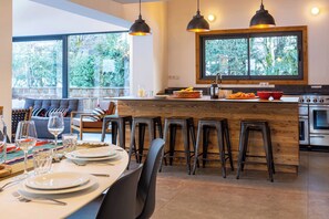 A modern kitchen with a central island, bar stools, and a dining area with a view of the outdoors. - Chalet Gloribel, ski, views, Chamonix All Year (Chamonix)