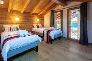 A room with two beds, wooden ceiling beams, and a large sliding glass door leading to an outdoor area.