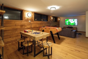 A cozy room with a foosball table, a foosball table in the corner, and a television on the wall.