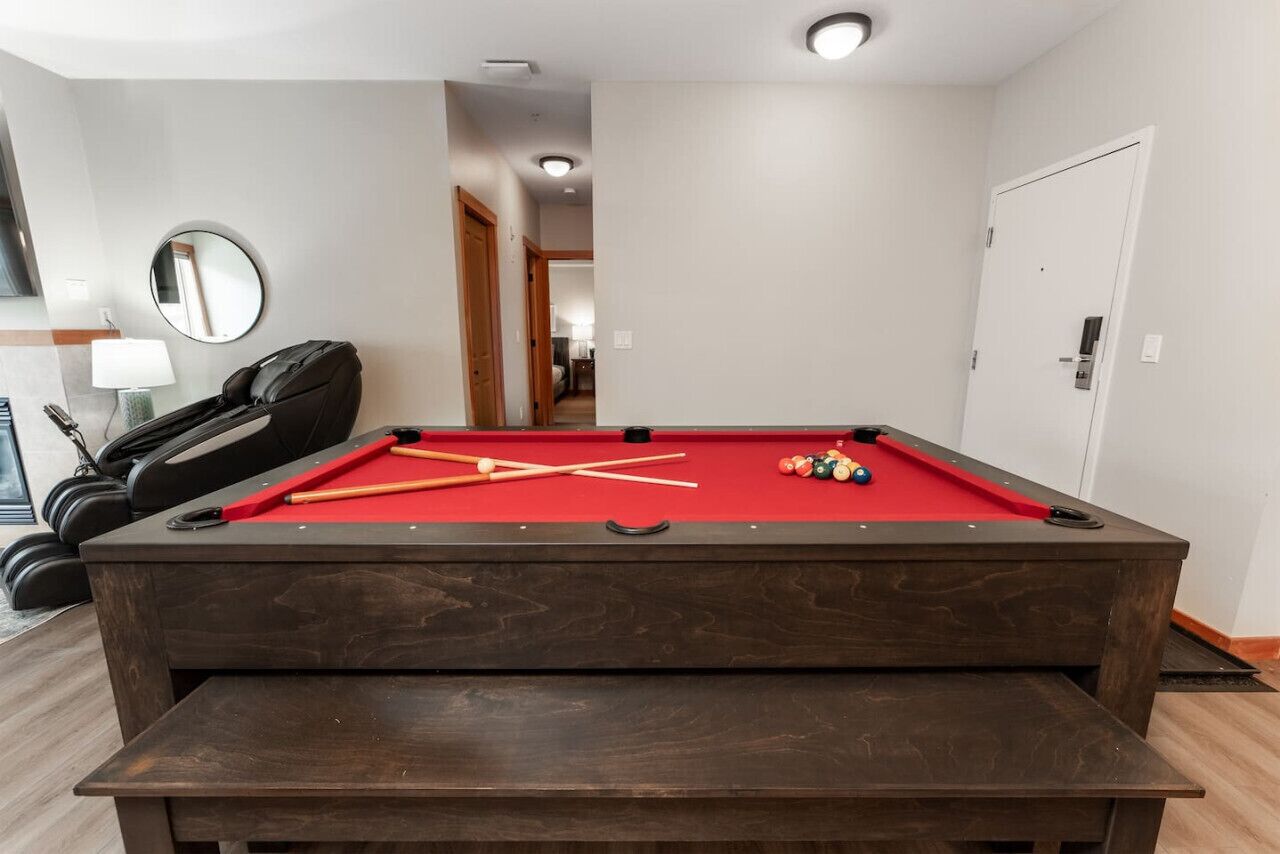 Una mesa de billar con superficie de fieltro rojo, rodeada por una mesa de madera oscura.