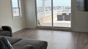 A spacious living room with a large sliding glass door leading to a balcony, a ceiling fan, and a flat-screen TV mounted on the wall.