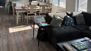 A spacious living area with a dark grey sofa, a coffee table with a puzzle, and a dining area with a white table and chairs.