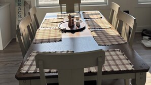 A dining area with a wooden table and chairs, a chandelier, and a view of a house through large windows.