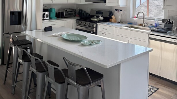 A modern kitchen with white cabinetry, stainless steel appliances, a central island with bar stools, and a view to the outside.