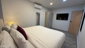 A hotel room with a bed, a wardrobe, a television, and an air conditioning unit.