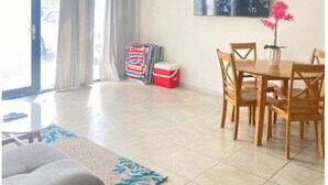 Ein geräumiger Wohnbereich mit Esstisch und Stühlen, einer Couch, einem an der Wand befestigten Fernseher und Blick durch das Fenster.