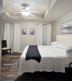 A bedroom with a bed, a chair, a ceiling fan, and two framed pictures on the wall. - Clean, Spacious. Newly renovated Garden Home in the heart of Pensacola.  (Pensacola)