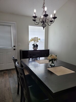 A dining area with a dark wooden table, chairs, a chandelier, and a window with white flowers. - Clean, Spacious. Newly renovated Garden Home in the heart of Pensacola.  (Pensacola)
