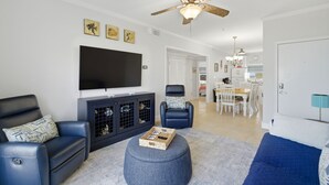 Una sala de estar con televisor de pantalla plana, ventilador de techo y comedor con mesa y sillas.