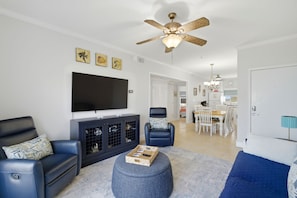 A living room with a flat-screen TV, a ceiling fan, and a dining area with a table and chairs.