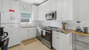 Una cocina con gabinetes blancos, un refrigerador de acero inoxidable, un microondas, un horno, una cafetera y una licuadora en la encimera.