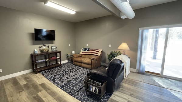 A living room with a brown sofa, a black leather chair, a TV mounted on the wall, and a patterned rug. - Munds Park - Beautiful Munds Park Suite for Rent. Newly built! (Sedona)