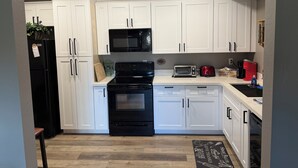 A modern kitchen with white cabinets, a black stove, a microwave, a toaster, and a coffee maker. - Munds Park - Beautiful Munds Park Suite for Rent. Newly built! (Sedona)