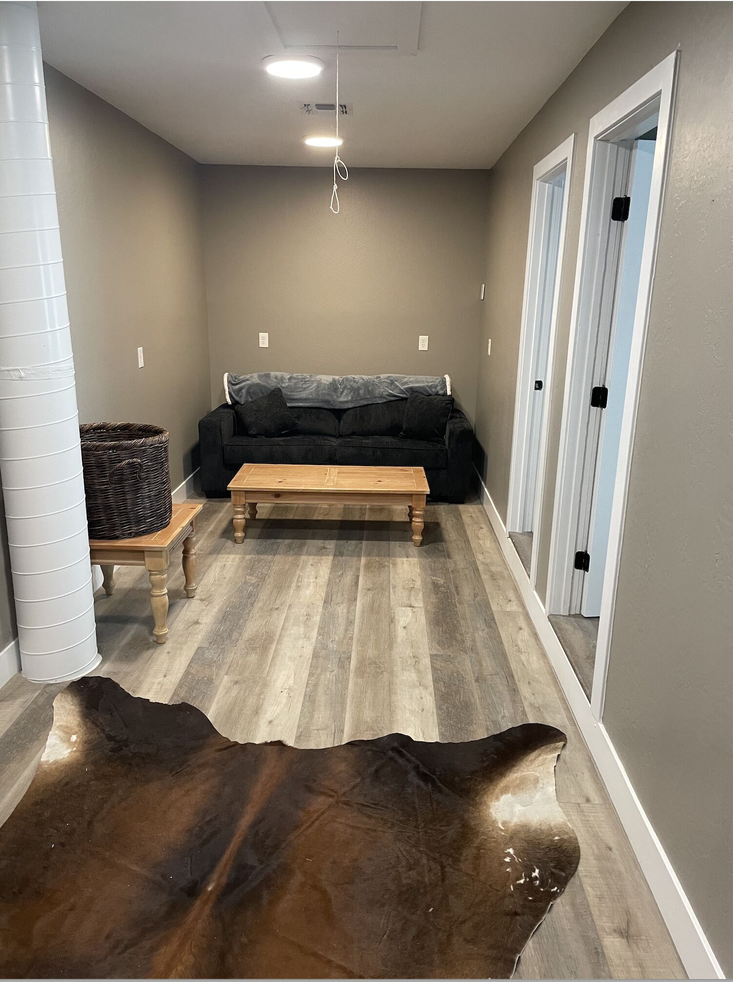 A room with a wooden floor, a black sofa, a wooden coffee table, and a large brown rug.