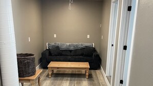 A room with a wooden floor, a black sofa, a wooden coffee table, and a large brown rug. - Munds Park - Beautiful Munds Park Suite for Rent. Newly built! (Sedona)