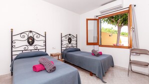 A room with two beds, a chair, and a window with a view of a tree.