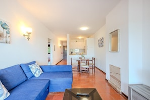 Una sala de estar con un sofá azul, una mesita de centro y una zona de comedor con una mesa y sillas.
