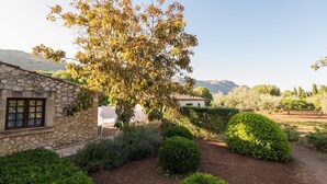 Un bâtiment en pierre doté d’une fenêtre, entouré de jardins bien entretenus et d’un grand arbre.