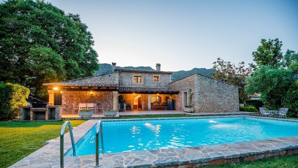 Une maison en pierre avec une piscine, un espace salon extérieur et une pelouse bien entretenue.