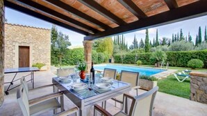 Une terrasse extérieure avec une table dressée pour le repas, une piscine et un bâtiment en pierre en arrière-plan.