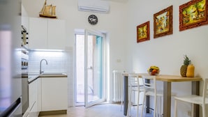 Une cuisine avec des meubles blancs, un four encastré, un évier et un coin repas avec des chaises et une table blanches.