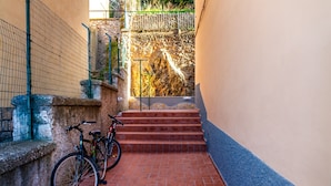 Un étroit sentier pavé de briques, avec un vélo appuyé contre un mur, qui mène à une série de marches en pierre.