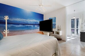 Quarto com um mural de vista ampla para o oceano, uma cama, um ventilador de teto e uma televisão.