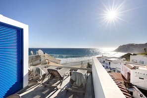 Un balcon avec des chaises longues, une vue sur la mer et un bâtiment avec une porte bleue.