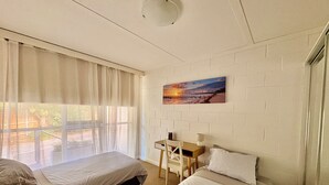 A room with two beds, a desk, a chair, a painting, and a window with curtains.