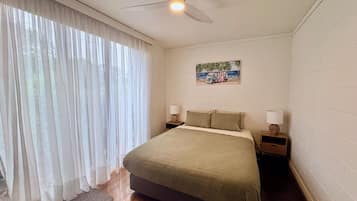A bedroom with a bed, two bedside tables, a ceiling fan, and a window with sheer curtains.