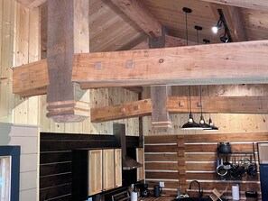 A kitchen with wooden beams, hanging pendant lights, and a pot rack.