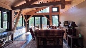 A spacious living room with a high ceiling, large windows, a leather armchair, a wooden coffee table, and a television. - Dragonfly - Unique, tranquil retreat in Grand Marais, MN (Grand Marais)