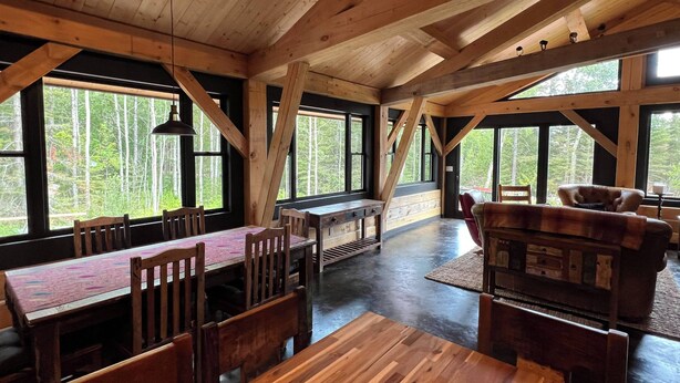 A rustic wooden interior with a dining area, large windows, and a cozy seating arrangement. - Dragonfly - Unique, tranquil retreat in Grand Marais, MN (Grand Marais)