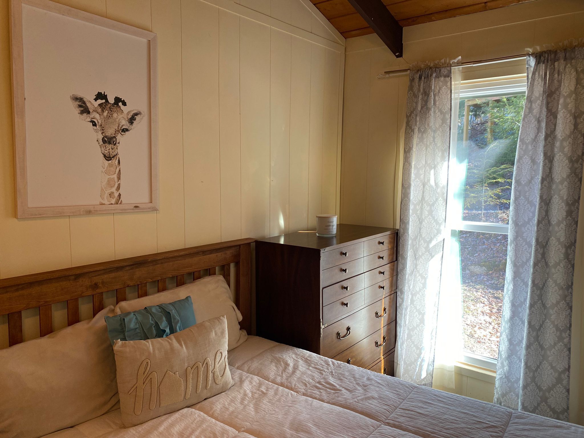 A bedroom with a bed, a dresser, a framed picture on the wall, and a window with curtains.