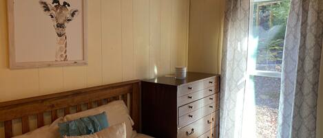 A bedroom with a bed, a dresser, a framed picture on the wall, and a window with curtains.