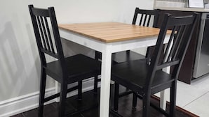 A dining table with four chairs, a kitchen area with cabinets and a refrigerator, and a wall-mounted light switch. - Zen Nest - Cozy, conveniently located, and just minutes to the airport! (Brampton)