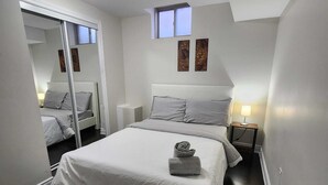 A modern bedroom with a large bed, a small window, and a mirror. - Zen Nest - Cozy, conveniently located, and just minutes to the airport! (Brampton)