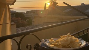 Un balcón con una fuente de papas fritas y vista al atardecer sobre un barrio residencial.