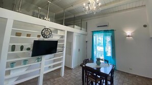 Un comedor con una mesa y sillas, un televisor sobre un estante blanco y una araña.