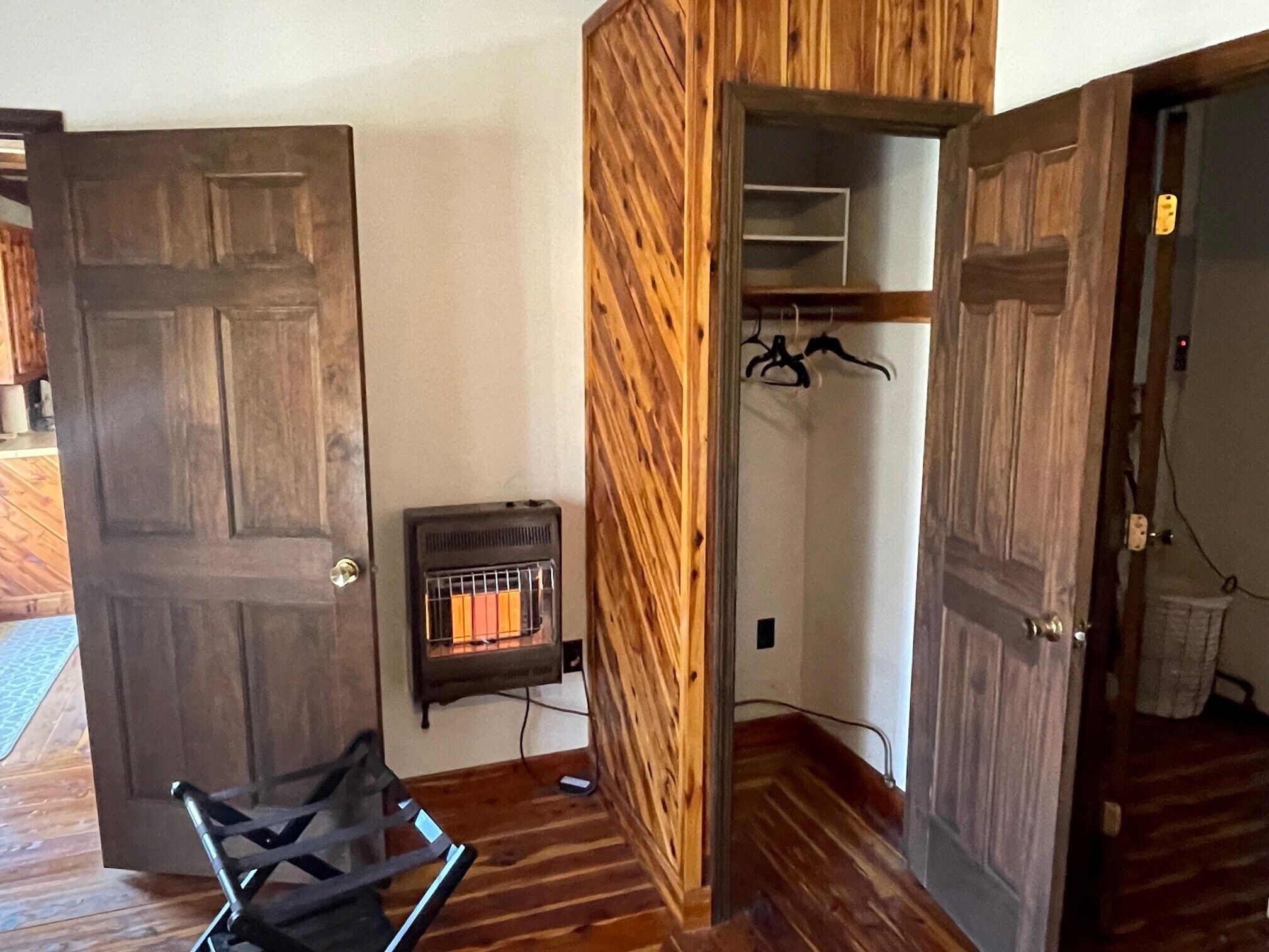 Una habitación con suelo de madera, un radiador, un perchero y una puerta que da a otra estancia.