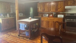 Une cuisine avec des meubles de rangement en bois, une table à manger en bois, un four à micro-ondes, un grille-pain et une machine à café.