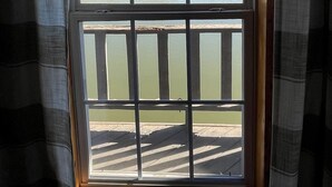 Une fenêtre donnant sur un plan d’eau et une terrasse en bois.